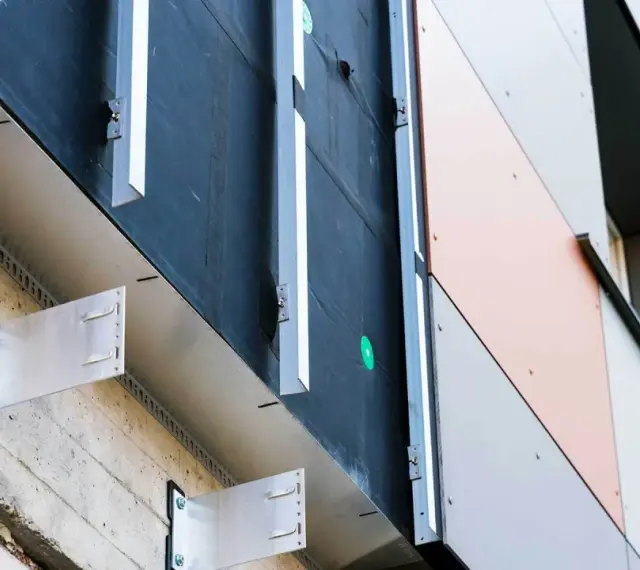 System mocowania paneli elewacyjnych. Widoczna betonowa ściana, izolacja i aluminiowe wsporniki tworzące przestrzeń dla wentylowanej elewacji.