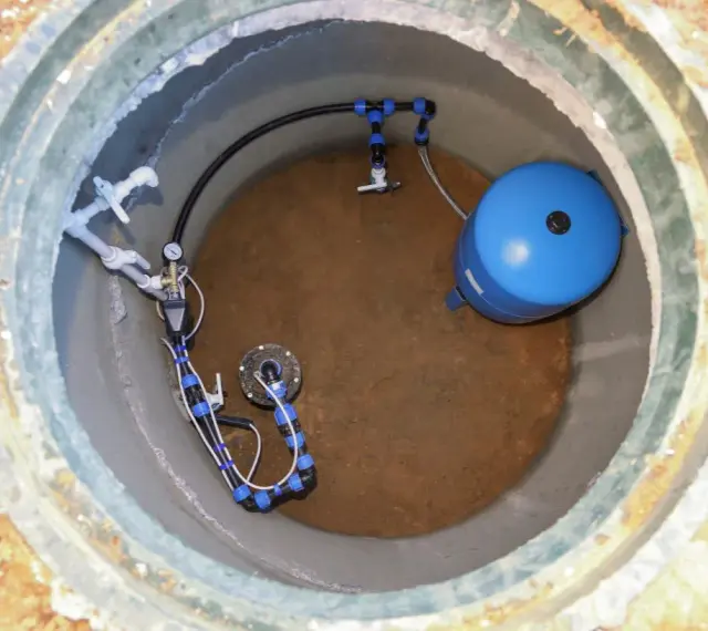 Wykończenie studni głębinowej: niebieski zbiornik hydroforowy i instalacja rurowa z manometrem.