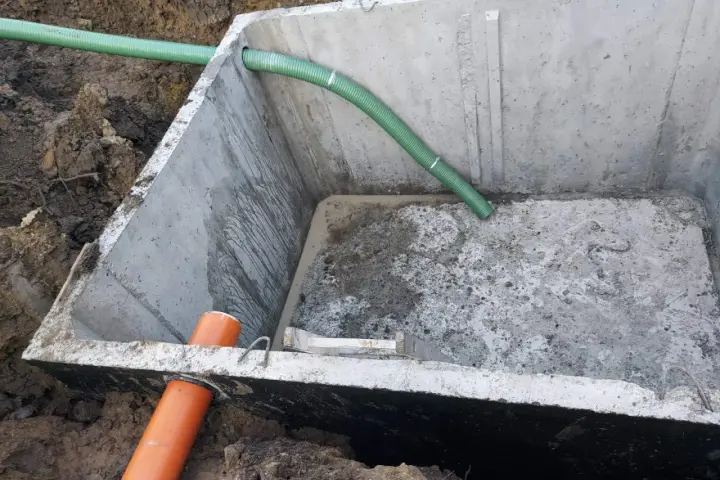 Szambo betonowe 10m3 cena z montażem. Instalacja wkopana w ziemię, widoczne rury doprowadzające.
