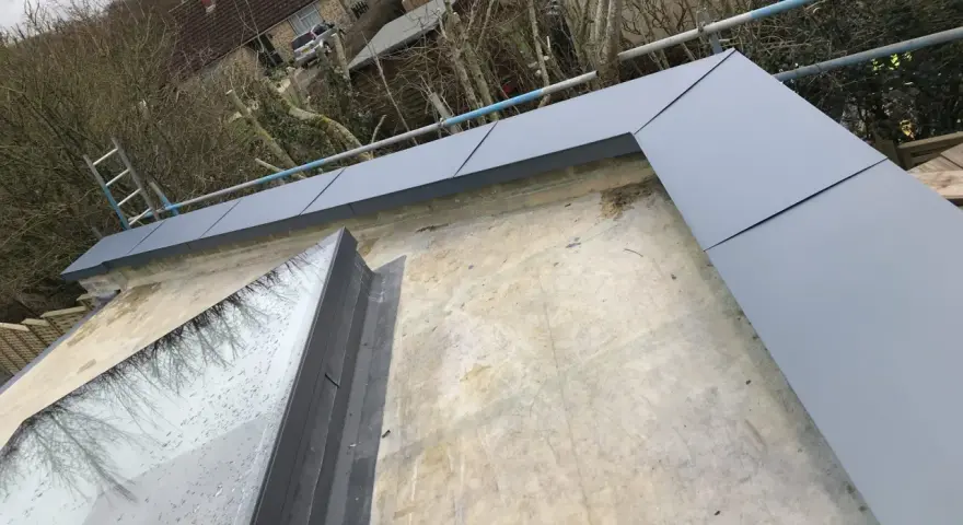 Nowoczesna attyka na dachu, z szarym wykończeniem, otacza okno dachowe. To rozwiązanie architektoniczne, które podnosi estetykę budynku.