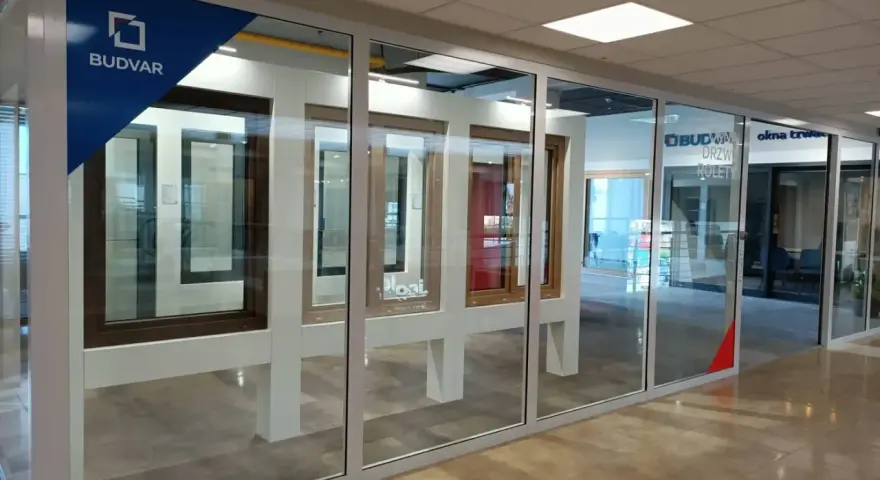 Salon okien i drzwi z ekspozycją okien i drzwi. Logo Budvar.