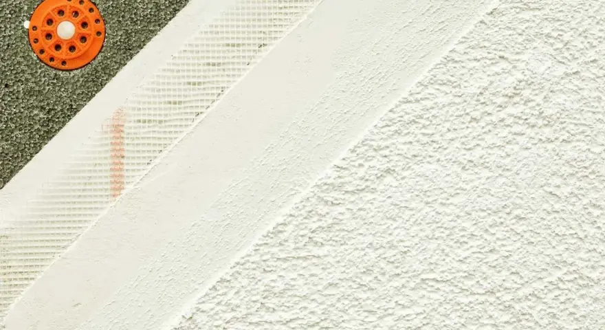 Warstwowa struktura elewacyjna: zielony styropian z pomarańczowym kołkiem, siatka zbrojeniowa i biały tynk.