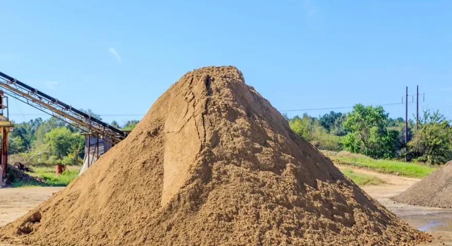 Duża hałda piasku na placu budowy, z taśmociągiem w tle.