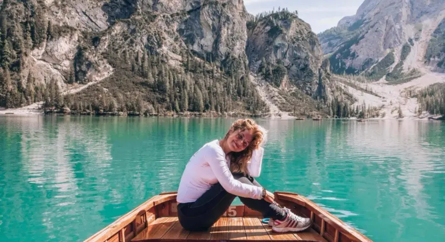 Uśmiechnięta kobieta siedzi w łodzi na turkusowym jeziorze, otoczona majestatycznymi górami **Dolomitów**.