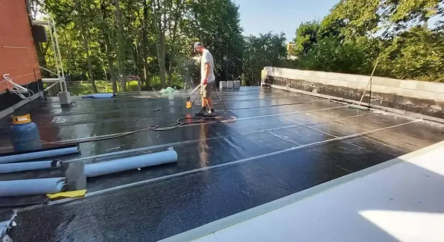 Pracownik wykonuje hydroizolację tarasu nad garażem, używając palnika do zgrzewania papy.