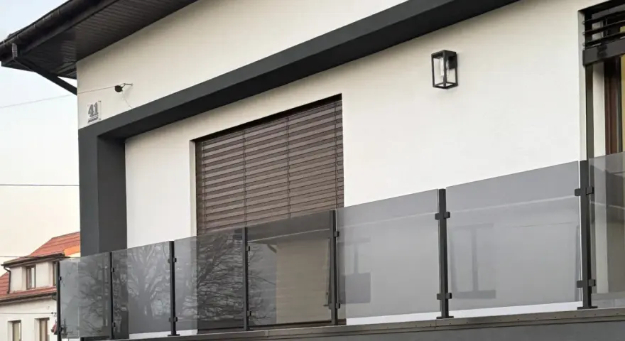 Nowoczesna balustrada z matowego szkła i czarnych słupków w kolorze RAL 9005, odbijająca drzewa.