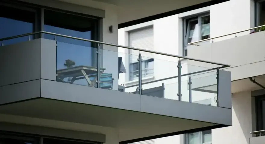 Nowoczesna loggia z przeszkloną balustradą, na której stoi stolik z kwiatami i krzesło.