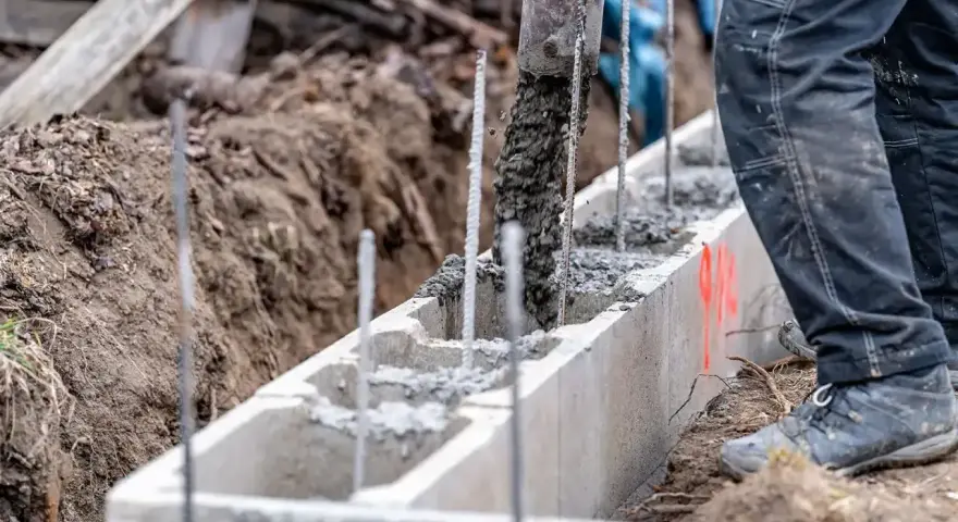 Betoniarka wylewa beton do szalunku. Pracownik w czarnych spodniach nadzoruje proces, który jest kluczowy, by wiedzieć, jak obliczyć kubik betonu.