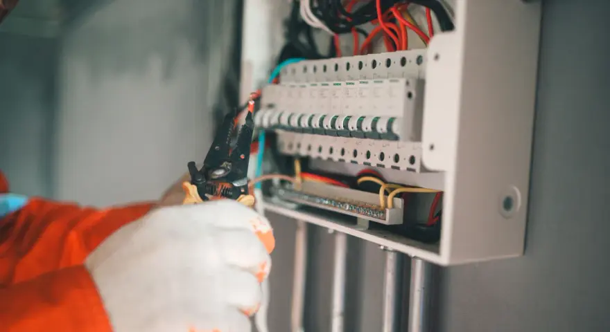 Elektryk w białych rękawiczkach montuje zabezpieczenie przedlicznikowe w skrzynce z bezpiecznikami.