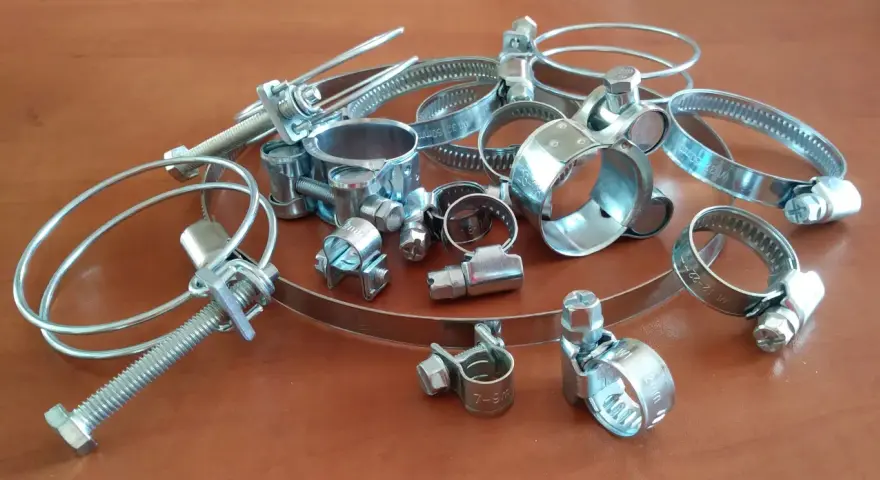 Metalowe opaski zaciskowe, czyli trytytki, w różnych rozmiarach, leżą na drewnianym blacie.