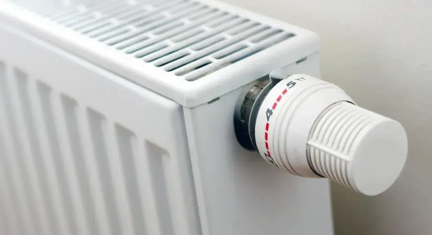 Biały grzejnik z termostatem. Różne rodzaje grzejników oferują różne sposoby regulacji temperatury.