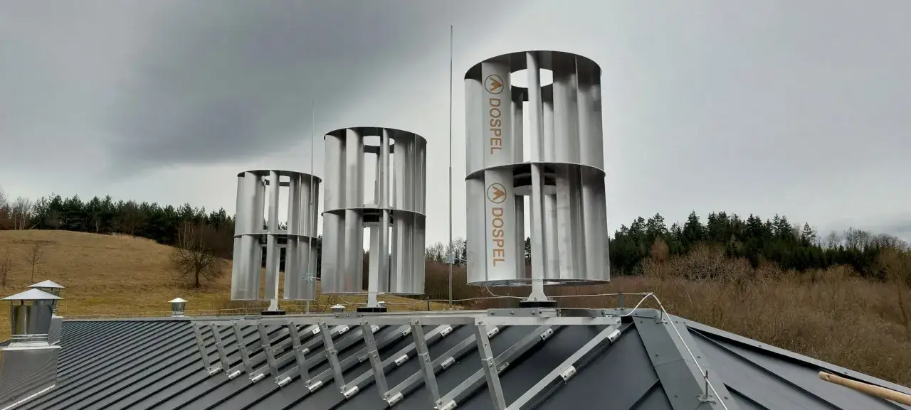 Na dachu zamontowano pionową elektrownię wiatrową Dospel. W tle las i wzgórza.