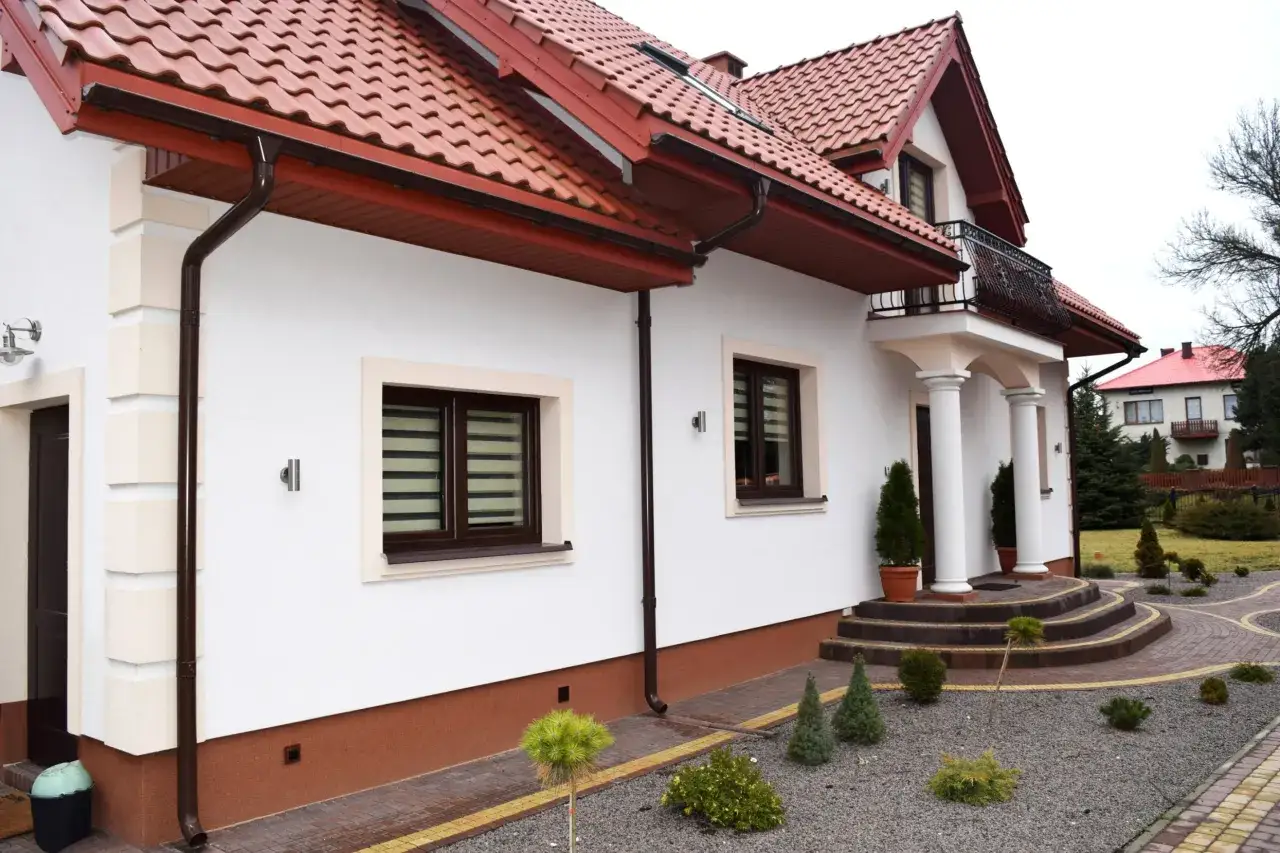 Elegancki cokół na elewacji domu, wykończony brązową farbą, chroni ściany przed wilgocią.