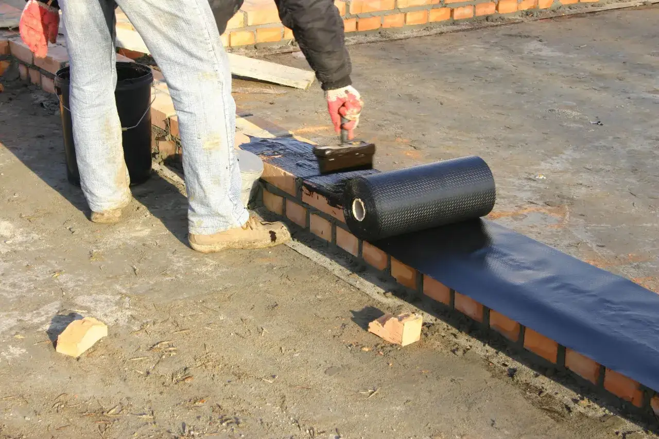 Pracownik nakłada na ceglany murek masę izolacyjną, przygotowując podłoże pod izoplast b.