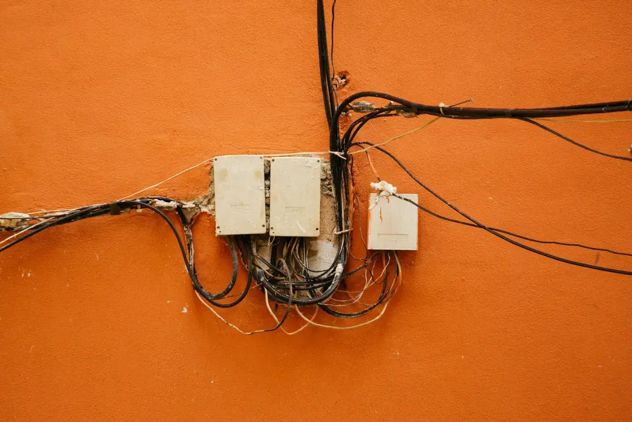 Skrzynki elektryczne i plątanina kabli na pomarańczowej ścianie. To ważny element uziemienia domu, zapewniający bezpieczeństwo.