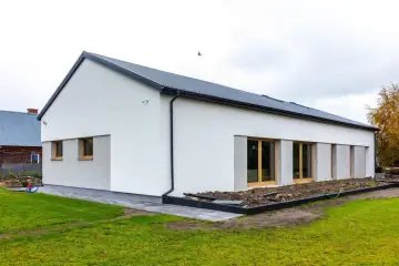 Nowoczesny dom z dachem dwuspadowym 100m2. Biała elewacja, duże okna, szary dach.