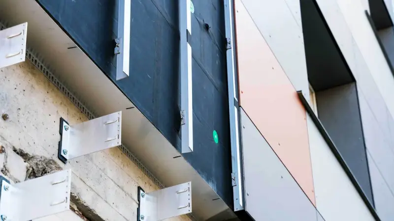 System mocowania paneli elewacyjnych. Widoczna betonowa ściana, izolacja i aluminiowe wsporniki tworzące przestrzeń dla wentylowanej elewacji.